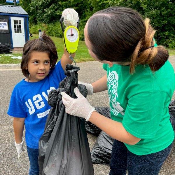 An adult and child weigh the amount of trash collected from a Grand Valley football game.