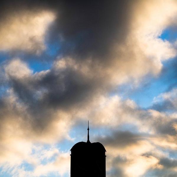 Silhouette of carillon tower against a blue sky with puffy clouds.