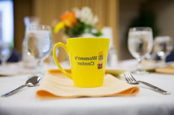 A yellow cup sits on a table setting. It reads "Women's Center" 